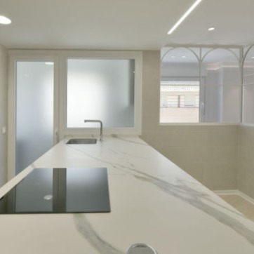 Puerta corredera de marco metálico negro con cristal, separando un dormitorio moderno de una biblioteca con estanterías llenas de libros. El dormitorio presenta un diseño elegante con paredes oscuras, cama de líneas minimalistas y una lámpara decorativa, mientras que la biblioteca combina funcionalidad y estilo contemporáneo.