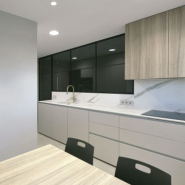 Cocina moderna con muebles blancos de líneas minimalistas, encimera de mármol blanco con vetas grises, y un grifo dorado sobre el fregadero. Al fondo, un cerramiento metálico negro con cristal que aporta un estilo contemporáneo, acompañado por muebles superiores de madera clara y un área de comedor en primer plano.