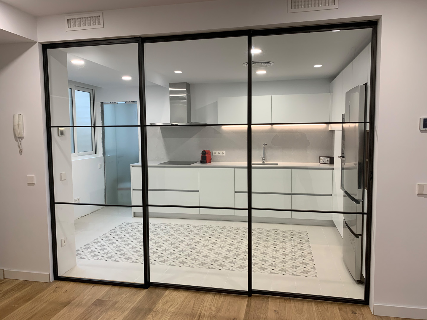 Interior moderno con puertas correderas de metal oscuro y cristal, conectando un salón elegante con un comedor amplio. Diseño minimalista con mobiliario contemporáneo, iluminación cálida y suelos de madera pulida.