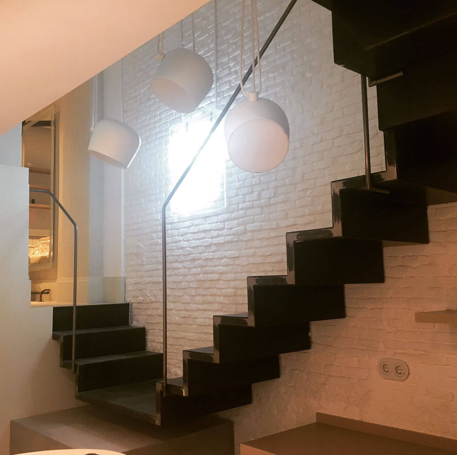 Detalle de una escalera moderna con estructura metálica y barandillas de cristal transparente. Los soportes y fijaciones de acero inoxidable añaden un diseño industrial elegante. La luz natural resalta los materiales y crea un ambiente luminoso y contemporáneo.